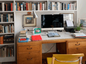 Picture of a desk with a computer on it, surrounded by a bookshelf