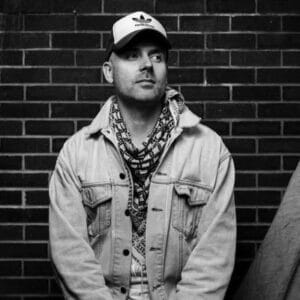 Black and white photo of a man in a hat standing against a brick wall