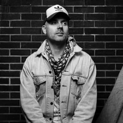 Black and white photo of a man in a hat standing against a brick wall